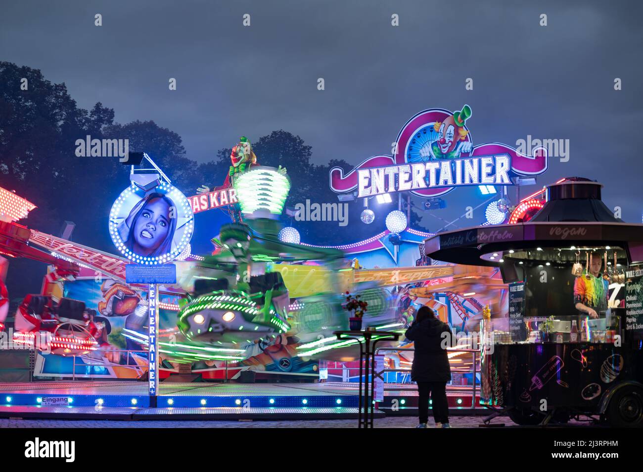 Entertainer-Funfair-Fahrt mit einem großen beleuchteten Logo am Abend. Die Fahrt auf dem Messegelände dreht sich sehr schnell. Freizeitaktivitäten in Deutschland. Stockfoto