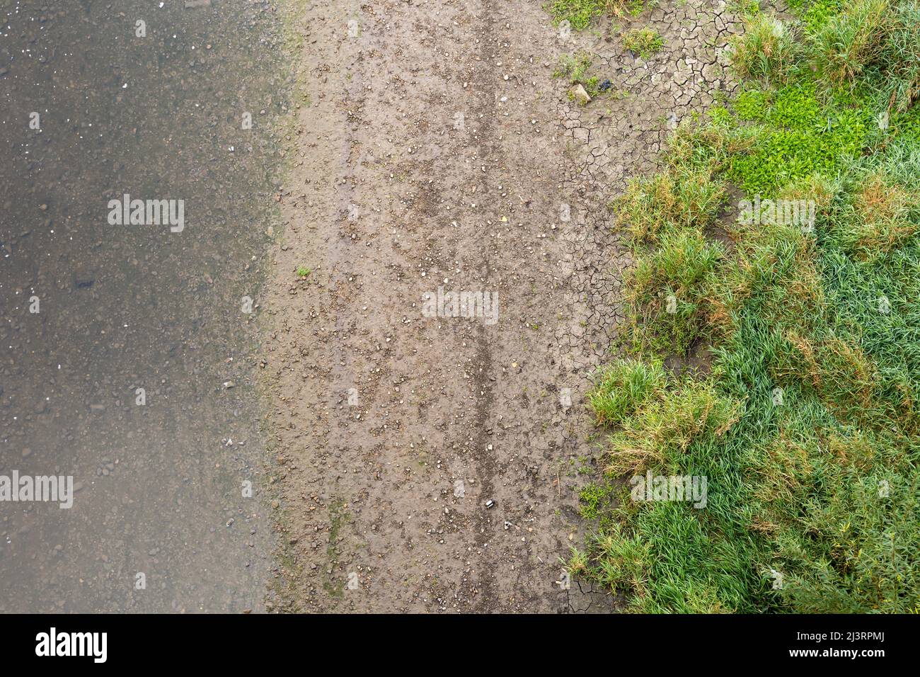 Blick von oben auf einen Fluss und ein Flussufer. Nasser Schmutz, kleine Steine und grünes Gras sind sichtbar. Das Wasser ist klar und unter Wasser sind Steine sichtbar. Stockfoto