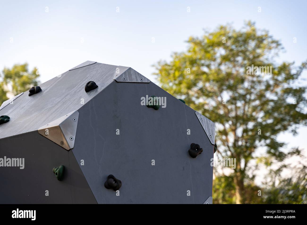 Spielplatzelement mit Kletterholds. Im Hintergrund befindet sich ein grüner Baum. Der Himmel ist blau und klar. Ausrüstung für sportliche Aktivitäten in einem öffentlichen Park. Stockfoto