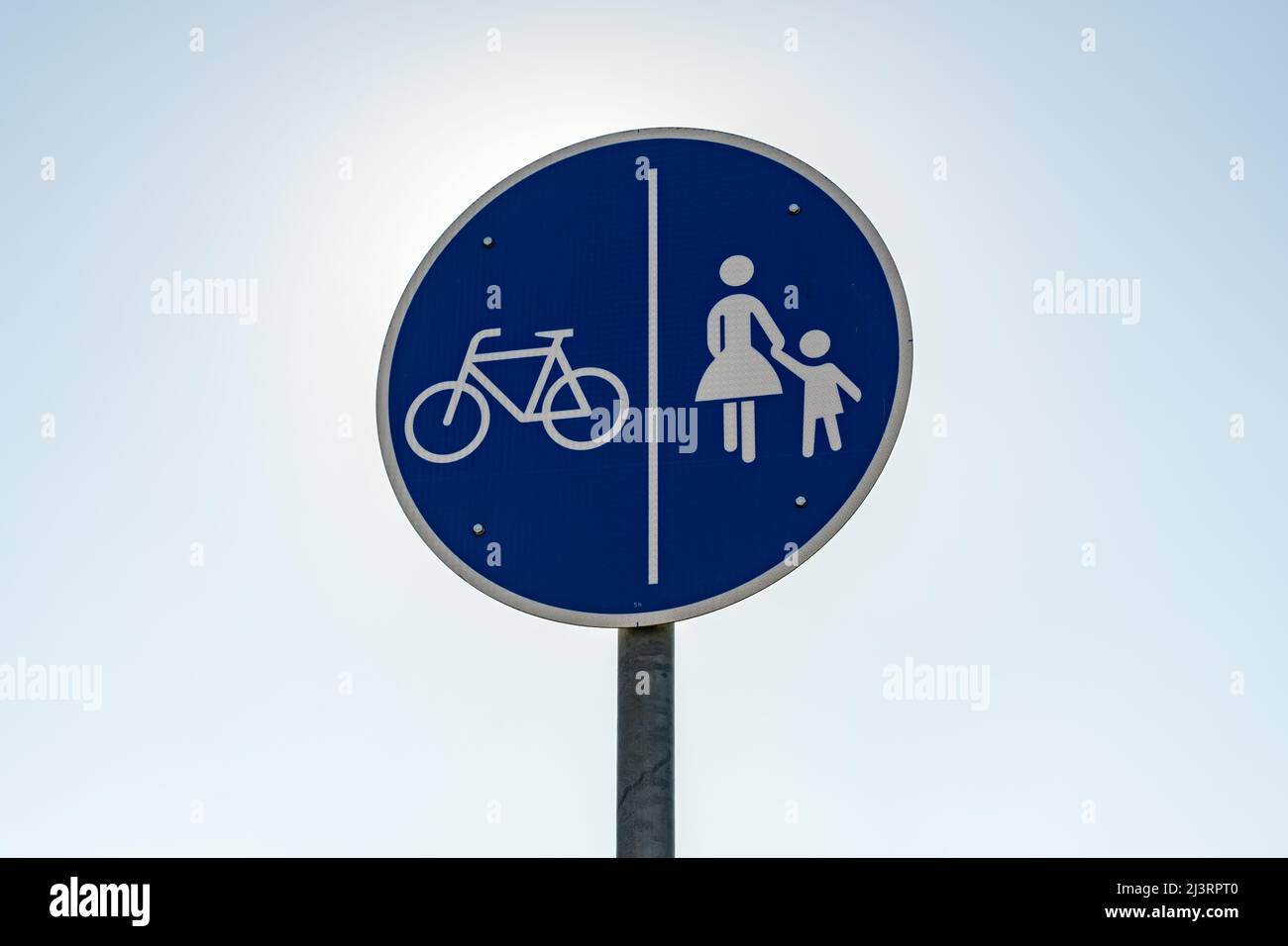 Ein Verkehrsschild mit gemeinsamem Pfad vor dem klaren blauen Himmel. Eine runde blaue Metallplatte in Deutschland. Dieses Symbol zeigt einen Pfad für Radfahrer und Fußgänger Stockfoto