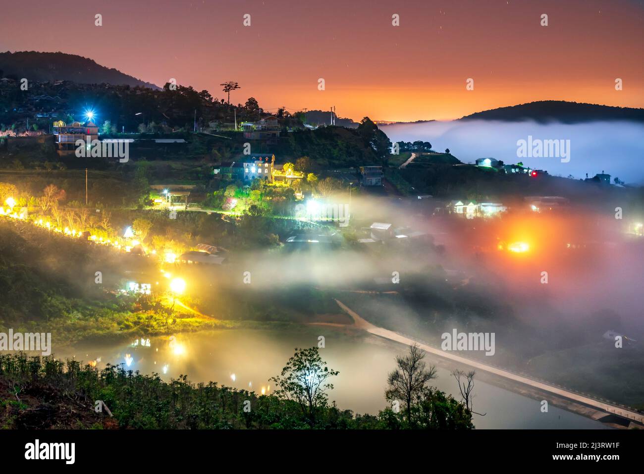 Nachtszene am Hang eine kleine Stadt im Nebel, umgeben von bunten Häusern und Lichtern, macht die Nacht im Hochland von Da Lat, Vietnam, so schön Stockfoto