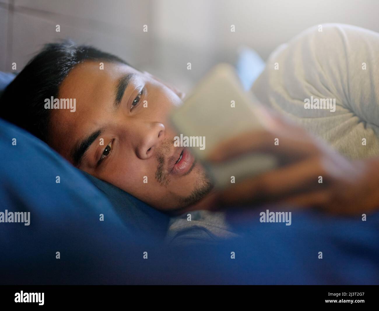 Social Media vom Bett aus. Aufnahme eines jungen Mannes, der im Bett liegend auf sein Telefon schaute. Stockfoto