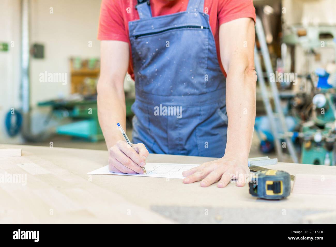 Unerkennbarer Zimmermann, der sich in einer hellen Werkstatt Notizen gemacht hat Stockfoto