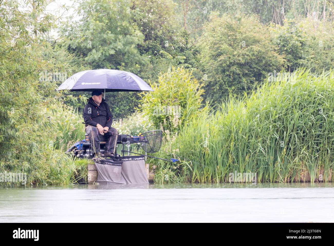 Mann, der im Regen unter einem Regenschirm fischt Stockfoto