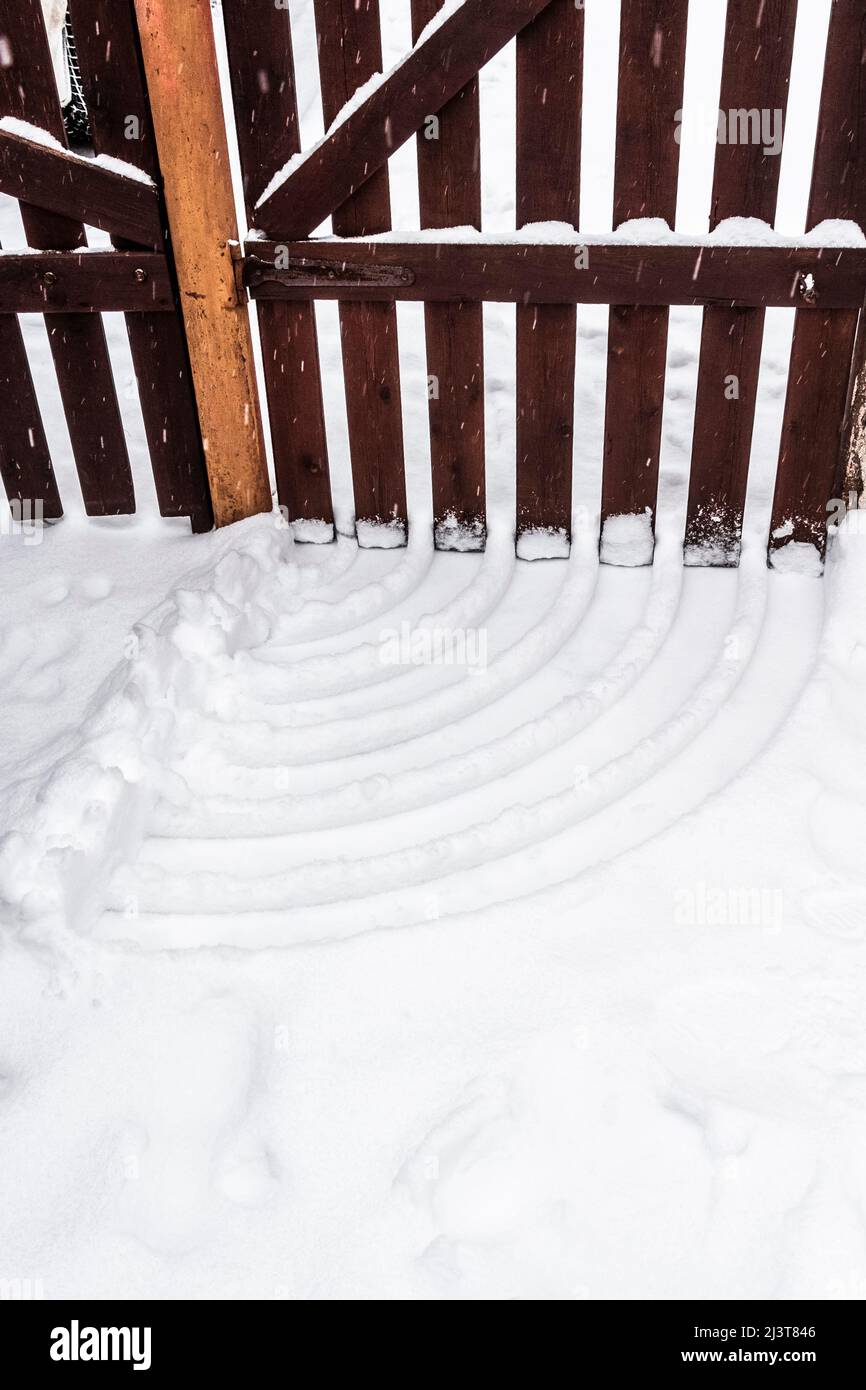 Furchen im Schnee in Form einer Wi-Fi-Ikone aus einem Holztor im Hinterhof eines Privathauses. Stockfoto