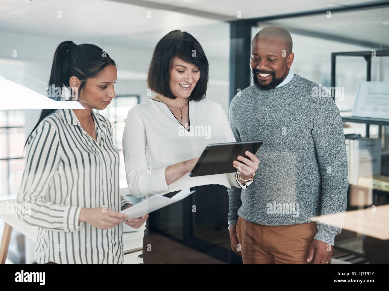 Die Leistungsbeurteilung sieht gut aus. Eine Kurzaufnahme einer vielfältigen Gruppe von Geschäftsleuten, die im Büro zusammenstehen und während einer ein Tablet verwenden Stockfoto