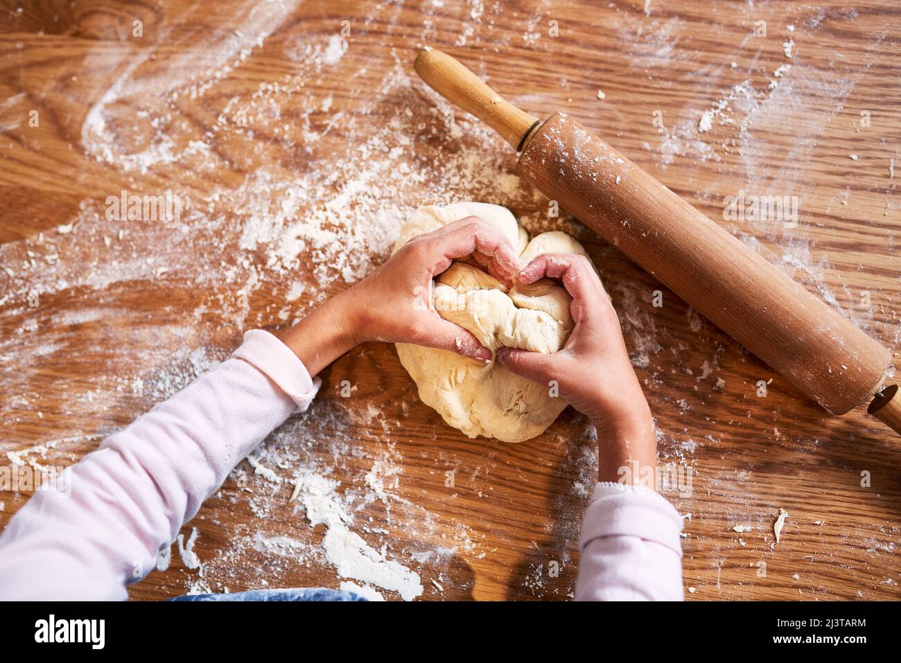 Rollen und Falten. Ein kleines Mädchen knetet Teig, während es zu Hause bäckt. Stockfoto