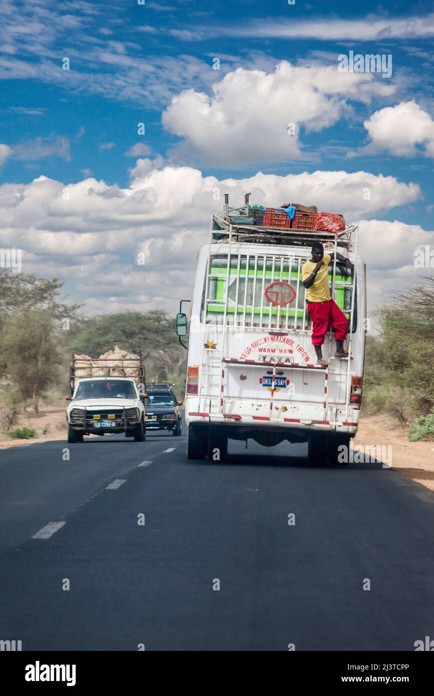 Senegal, Autobahnsicherheit. Mann, der einen Mango isst, während er sich auf einem Geländer auf der Rückseite eines Busses ausruht. Hier kein Sicherheitsgurt! Stockfoto