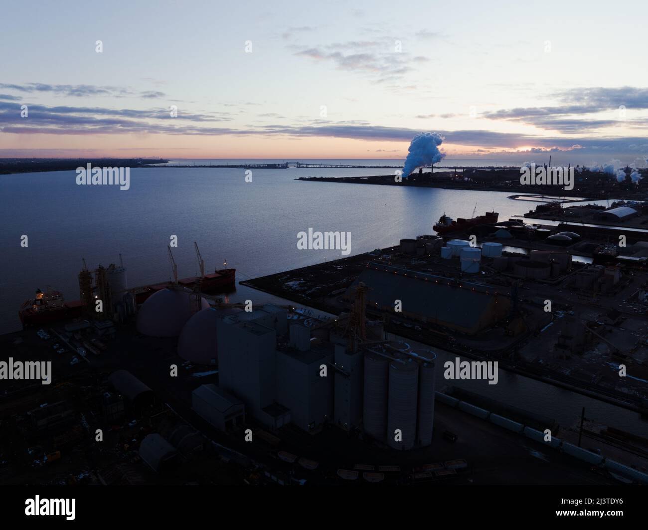 Die Sonne geht im Hintergrund auf, während eine Drohne eine Luftaufnahme über ein schattiges großes Industriegebiet und einen Seehafen in Kanada einfängt. Stockfoto