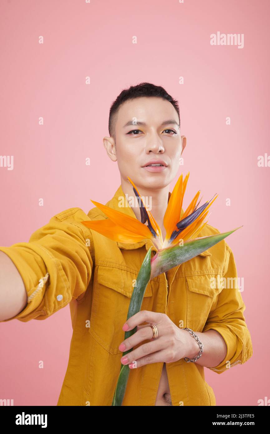 Vietnamesischer junger Mann mit farbenfrohem Make-up, der Selfie mit strelitzia-Blume in der Hand nimmt Stockfoto