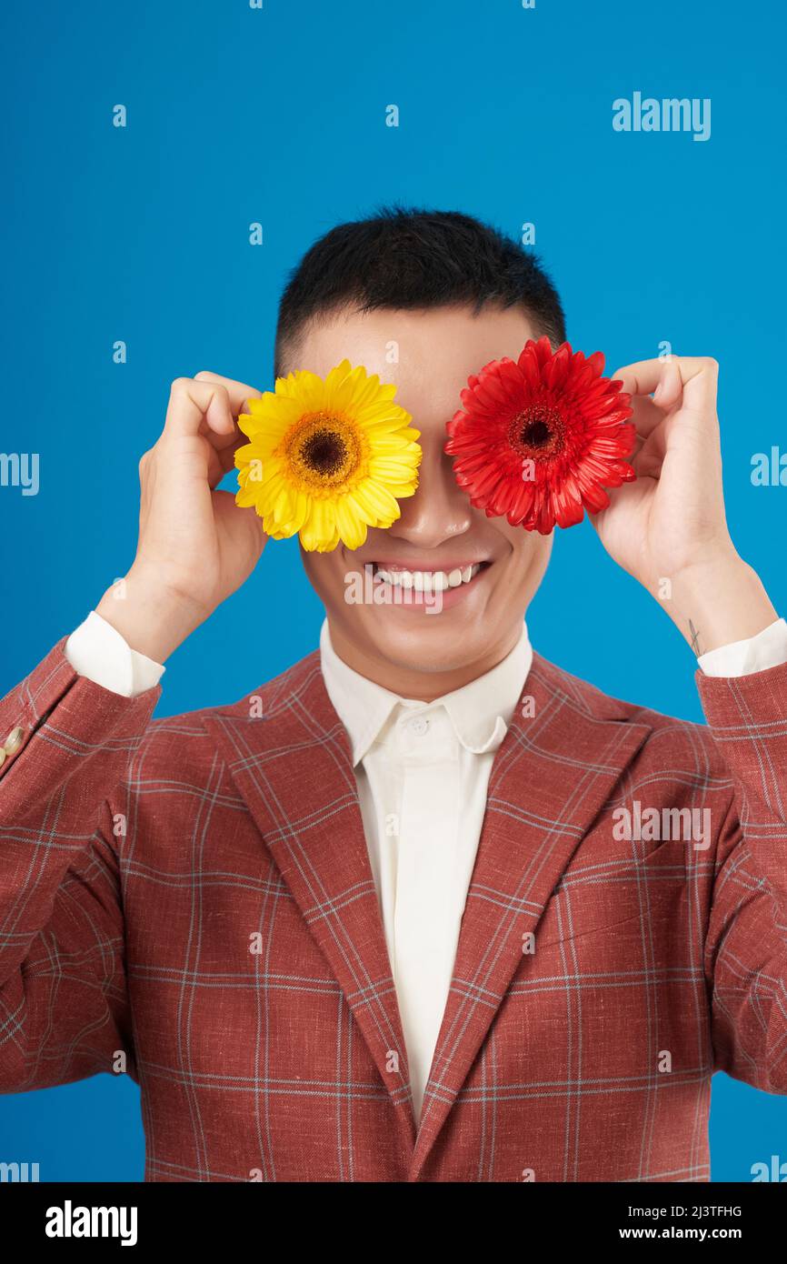 Porträt eines glücklichen jungen Mannes, der rote und gelbe Gänseblümchen vor den Augen hält Stockfoto