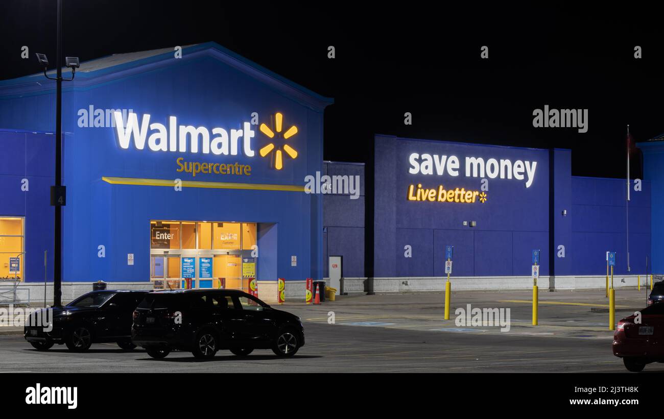 Die Vorderseite eines Walmart Superstore ist nachts abgebildet, ihr berühmter Slogan „Save Money, Live Better“ ist an der Seite des Gebäudes zu sehen. Stockfoto