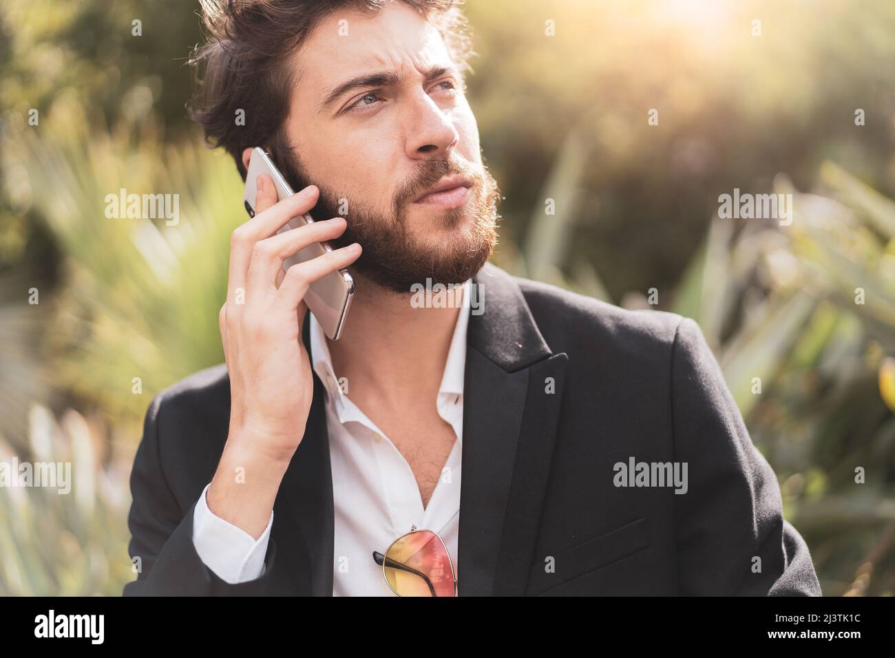 Hübscher bärtiger junger Mann im Anzug, der im Freien am Telefon telefoniert. Stockfoto