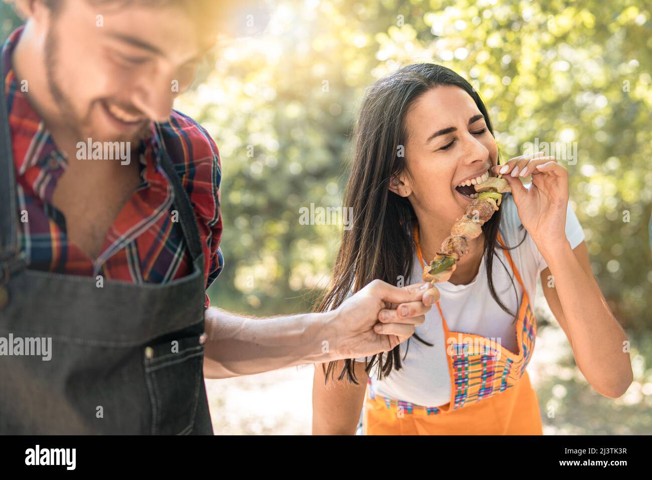 Eine junge Frau lacht, als sie während einer Reise auf dem Land Fleischspieße aus den Händen ihrer Freundin isst. Lifestyle-Konzept von jungen Erwachsenen mit Fu Stockfoto