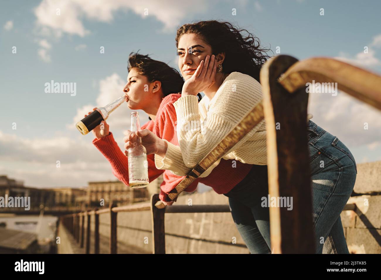 Die besten Freunde trinken Bier im Freien - zwei junge Frauen, die ihre Ellbogen an einem Geländer lehnen, trinken Bier und verbringen unbeschwert ihre Zeit mit entspannten Gesprächen Stockfoto