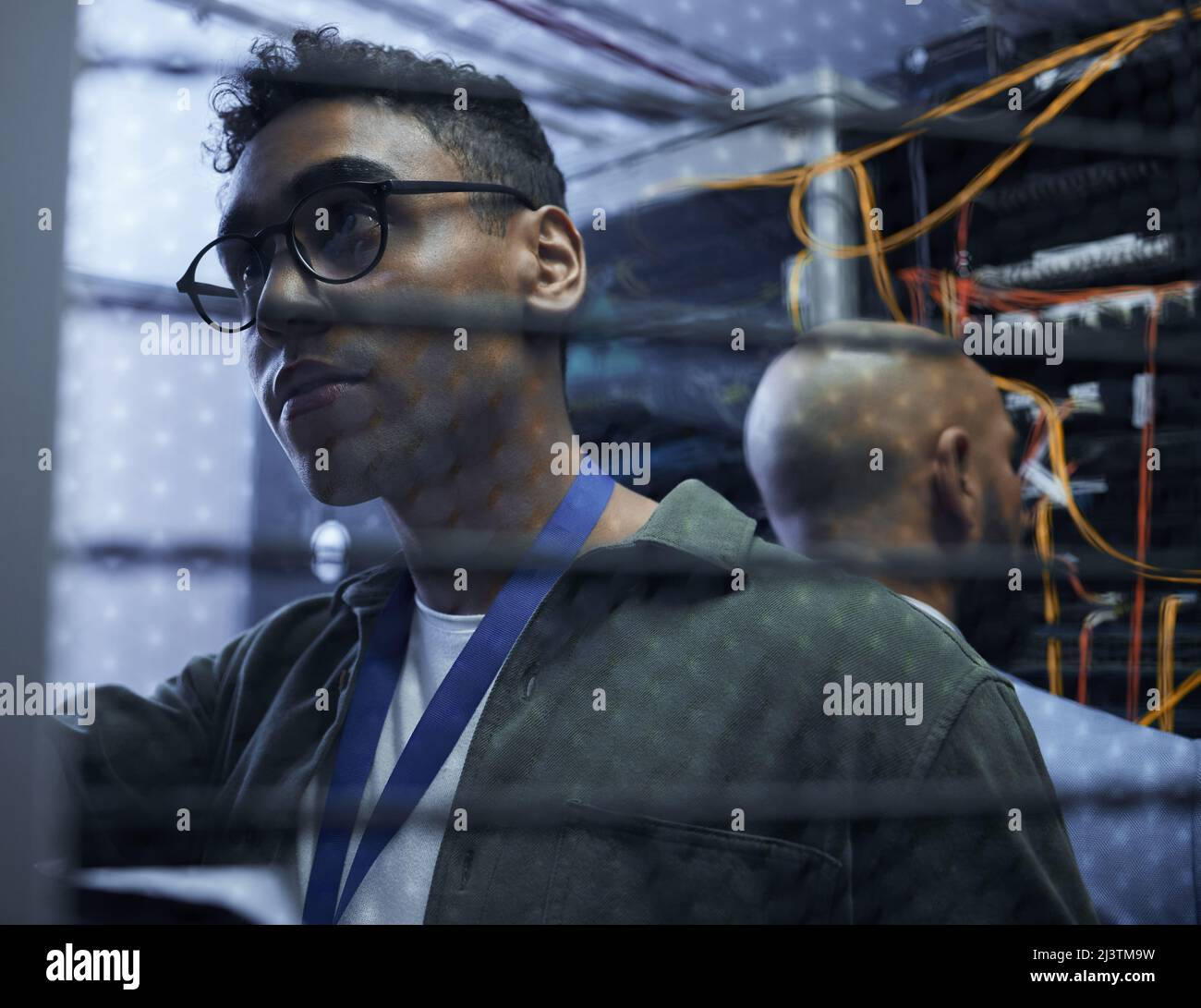 Sortieren des Servers. Eine kurze Aufnahme von zwei männlichen IT-Support-Agenten, die in einem dunklen Netzwerkserverraum zusammenarbeiten. Stockfoto