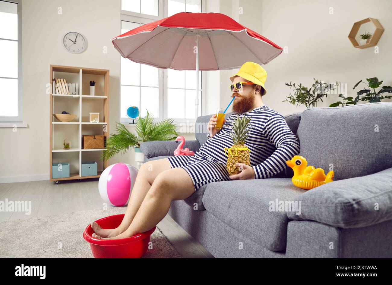 Der lustige Mann verbringt den Sommerurlaub zu Hause und sitzt auf dem Sofa, so als sei er am Strand. Stockfoto