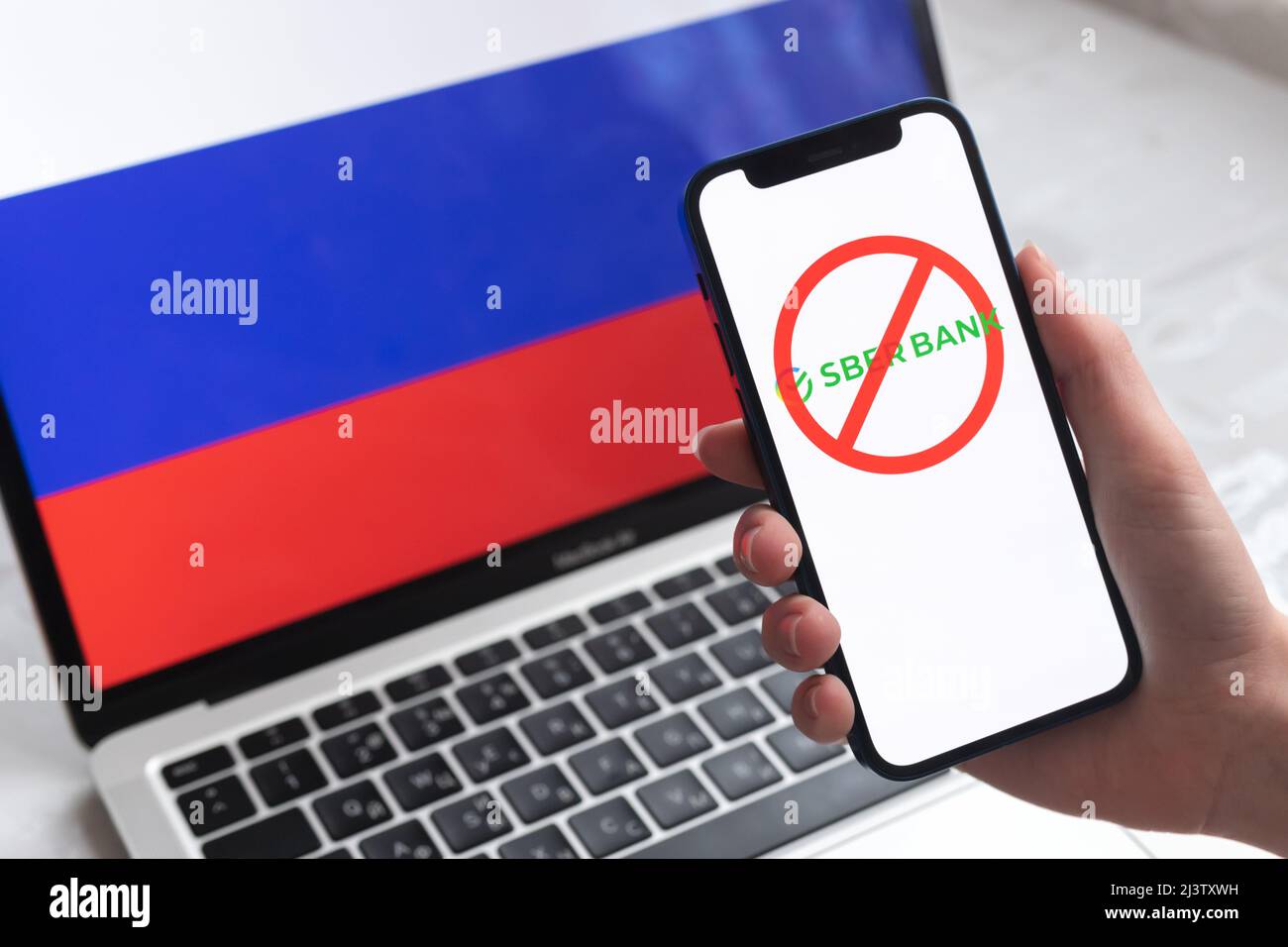 SPB, Russland - 8. April 2022: Sberbank und Sanktionen. Blockierte russische Bank, Logo und Ban-Symbol auf Handy-Bildschirm und Flagge Hintergrund Stockfoto