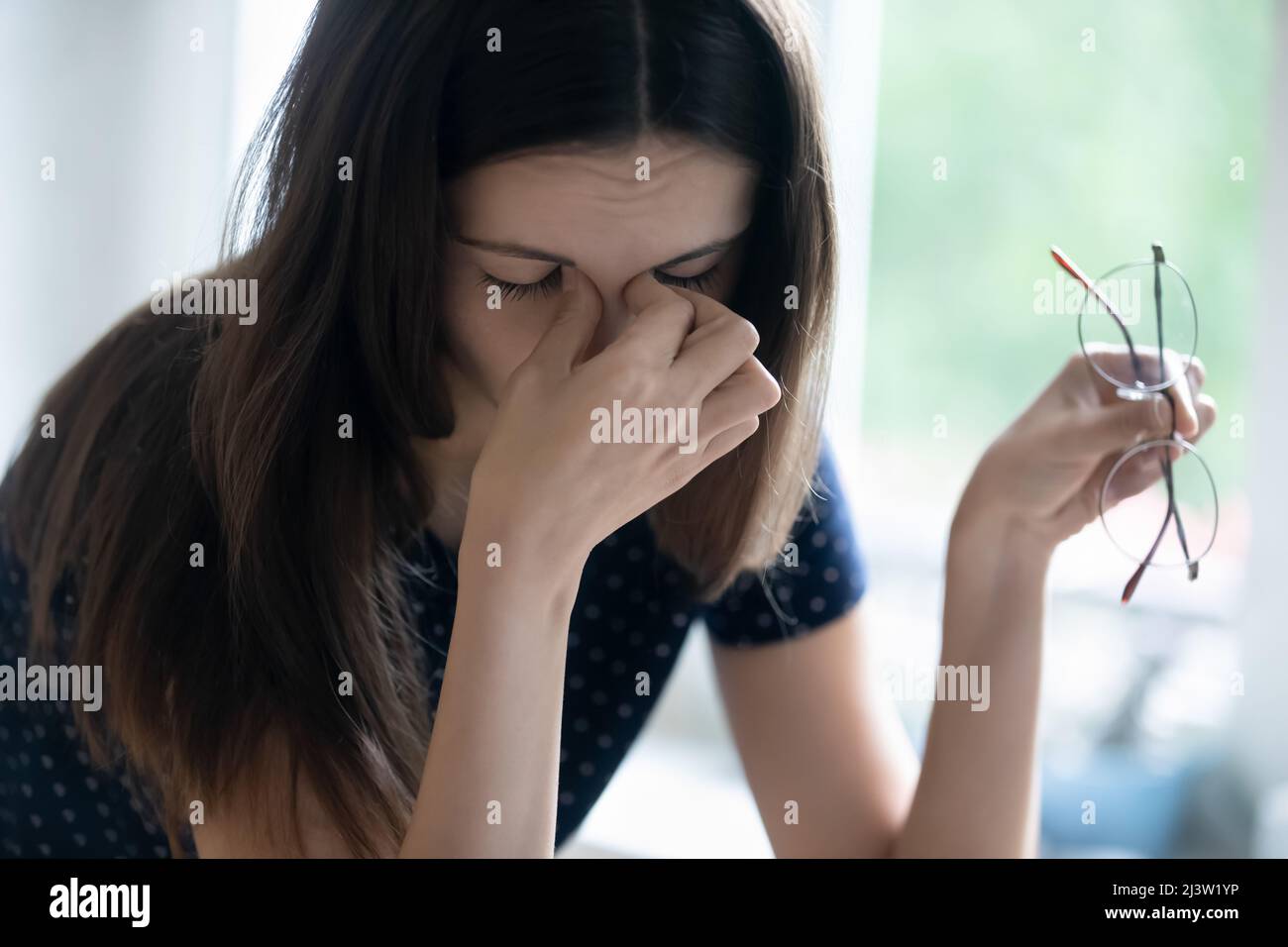 Junge Frau zieht die Brille aus, um die Augen zu belasten Stockfoto