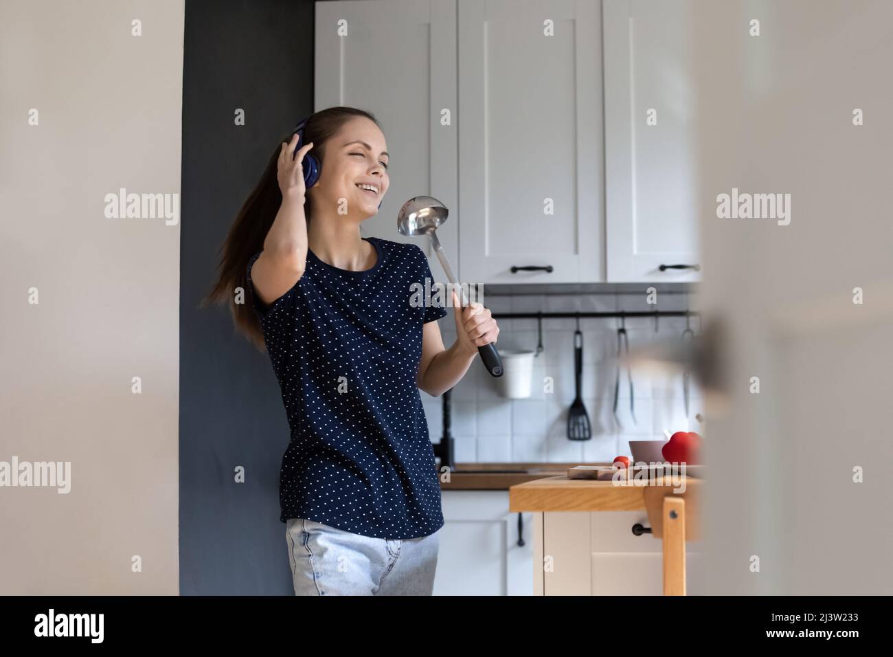Eine Frau in Kopfhörern hält die Schöpfkelle, als ob sich mike beim Singen sorglos anfühlt Stockfoto