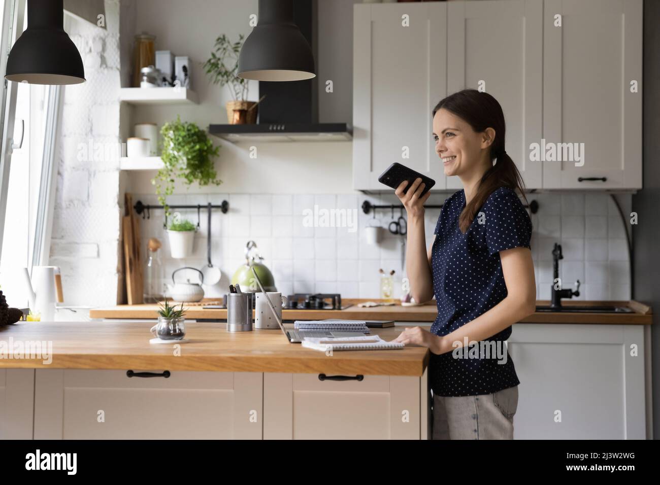 Frau, die in der Küche steht, verlässt die Sprachnachricht über das Mobiltelefon Stockfoto
