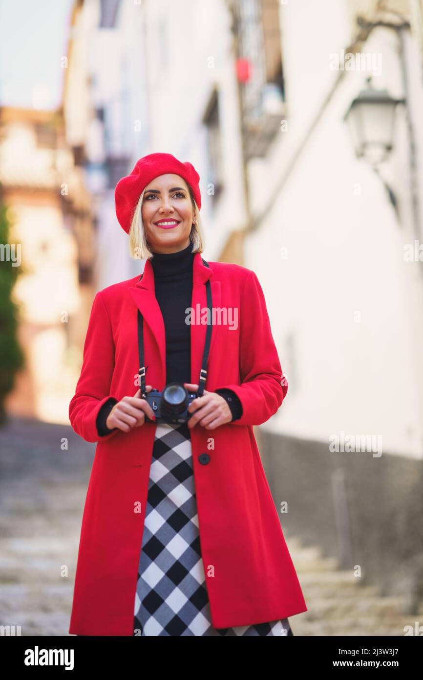 Lächelnde weibliche Touristin mit Fotokamera, die auf der Straße der Stadt auf der Treppe steht Stockfoto