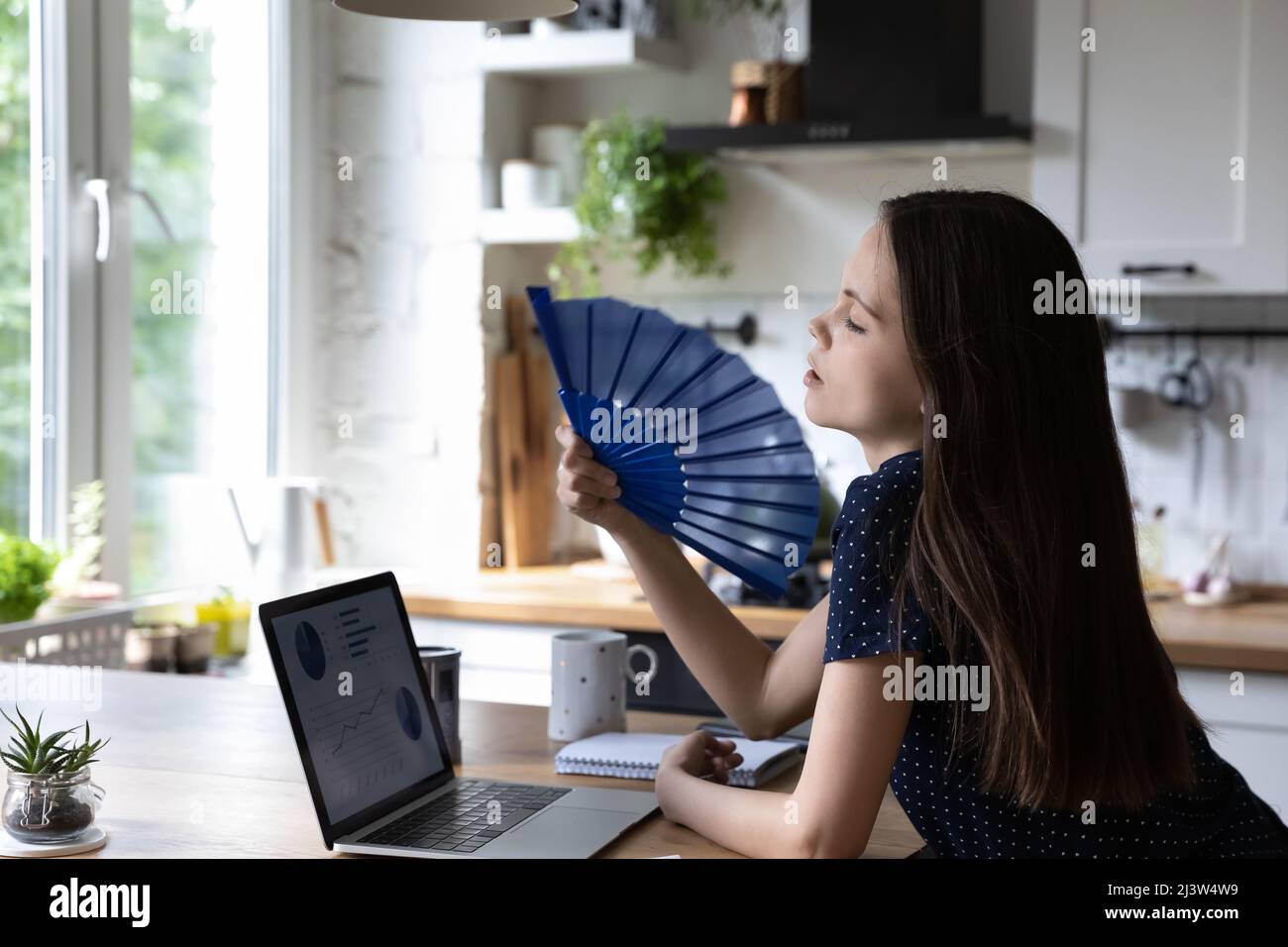 Die junge Frau kühlt sich zu Hause mit einem Handschwinger ab Stockfoto