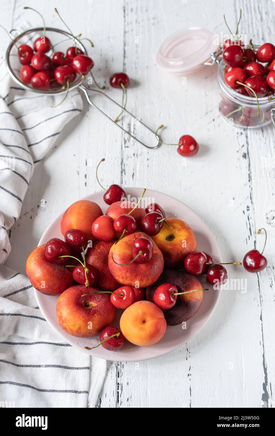 Frische reife Früchte auf Teller, Sieb und Glas auf weißem Holztisch Stockfoto