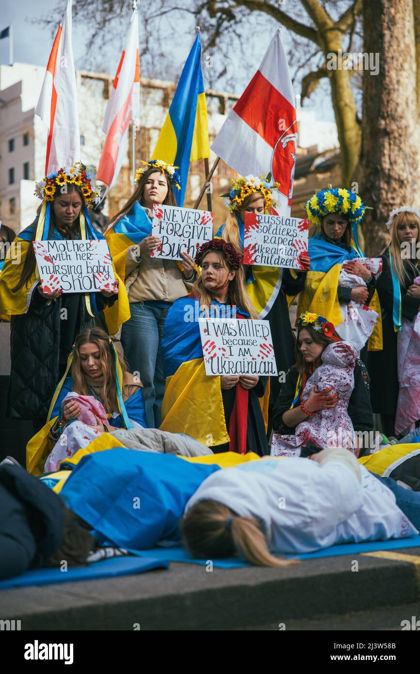 Eine Gruppe pro-ukrainischer Frauen demonstriert in London für den Krieg in der Ukraine. Umgeben von ukrainischen Fahnen, liegen auf dem Boden mit Blut bedeckt, Blumen Stockfoto