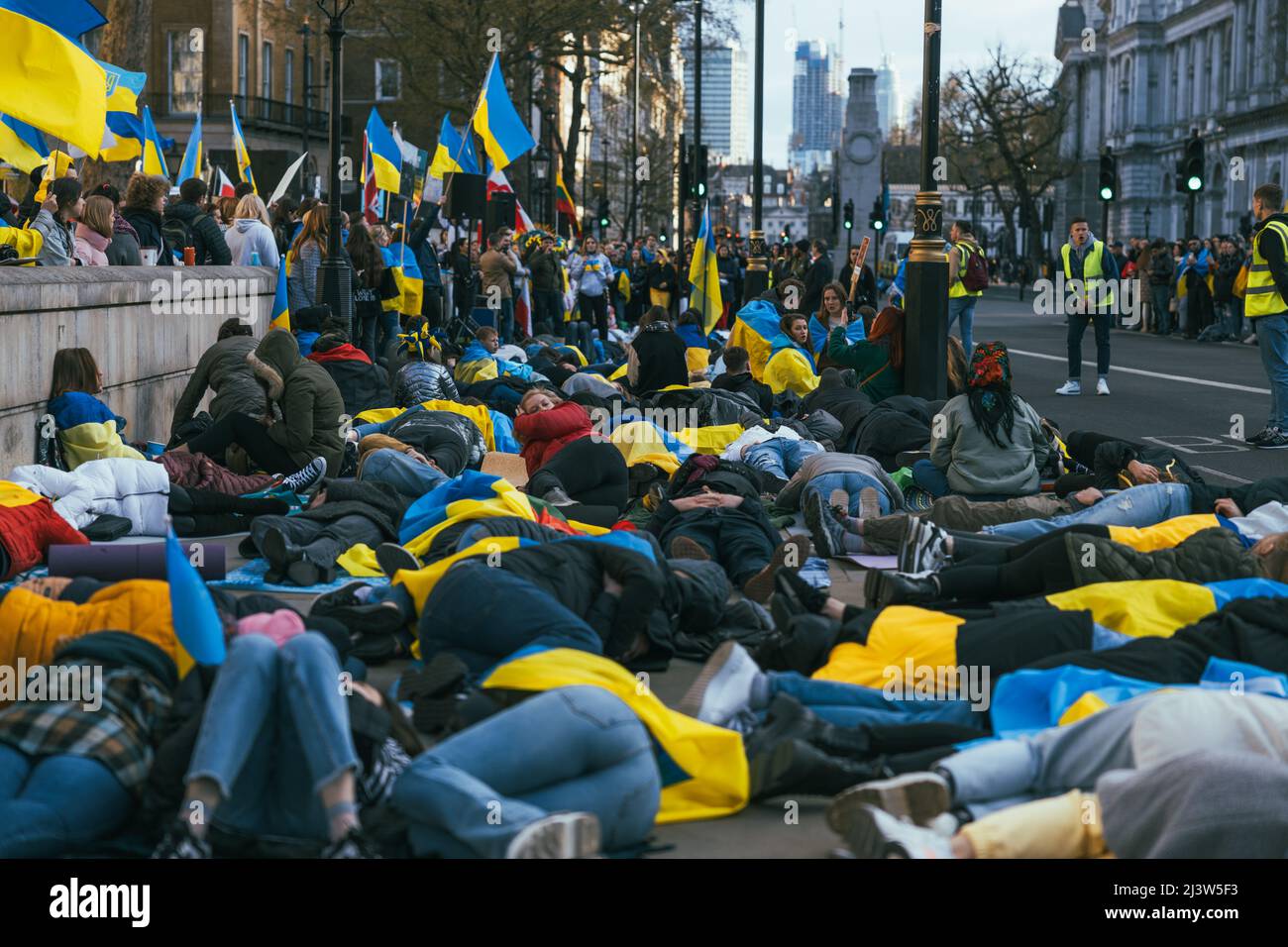 Aus Protest gegen den Krieg Russlands mit der Ukraine liegen Menschen auf dem Boden. Wir bitten darum, den Krieg inmitten ukrainischer Flaggen zu beenden. Demonstration gegen den Krieg Stockfoto