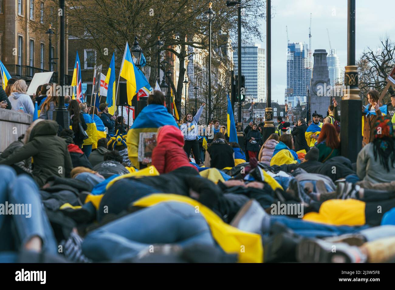 Hunderte von Menschen liegen als Protest gegen die russische Invasion auf dem Boden, während sie von ukrainischen Fahnen umgeben sind. Beendet den Krieg. Pro-Ukrainisch Stockfoto