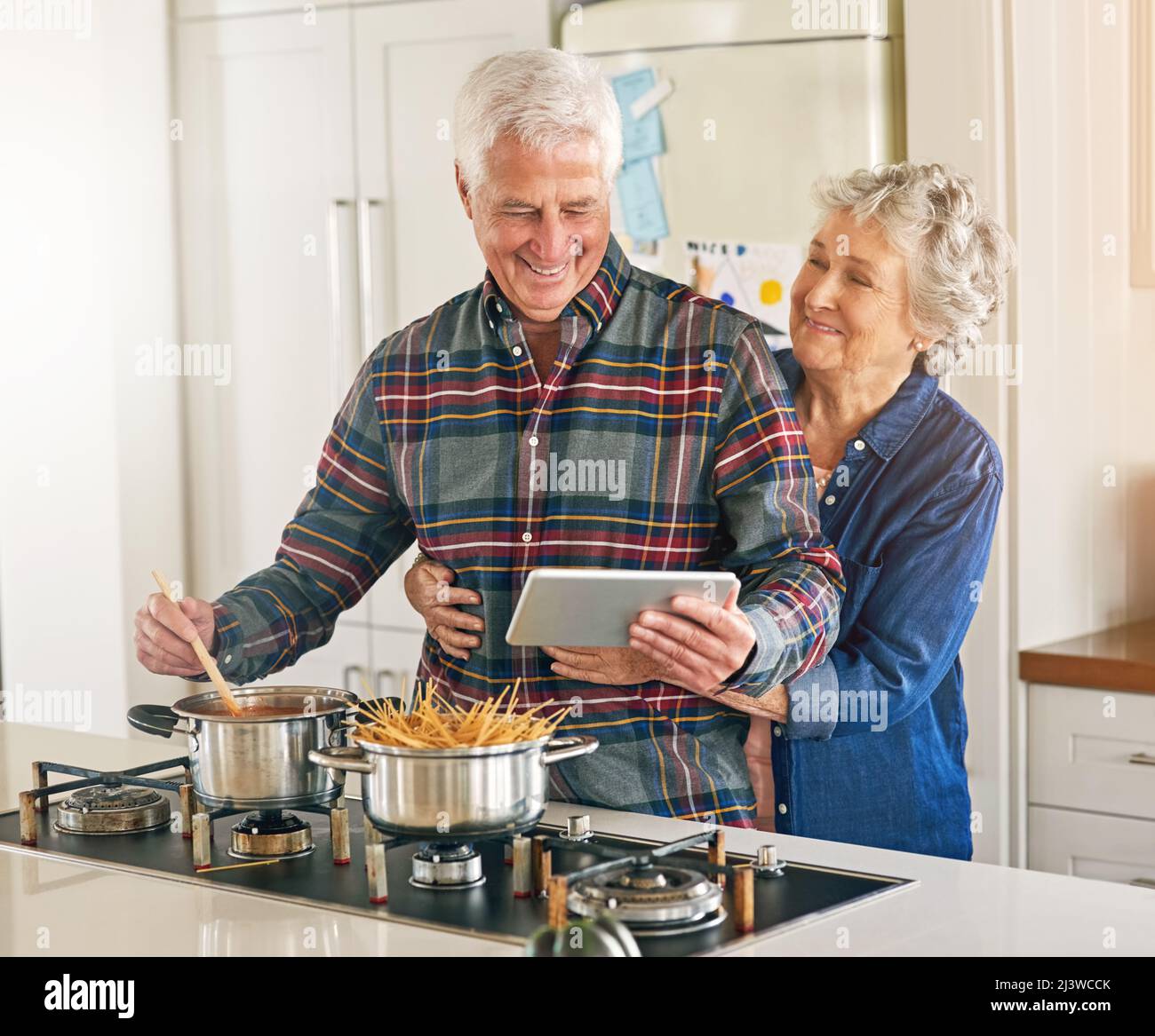 Was kocht, gut aussehend. Eine kurze Aufnahme eines älteren Ehepaares, das ein digitales Tablet verwendet, während es zu Hause in der Küche zusammen kocht. Stockfoto