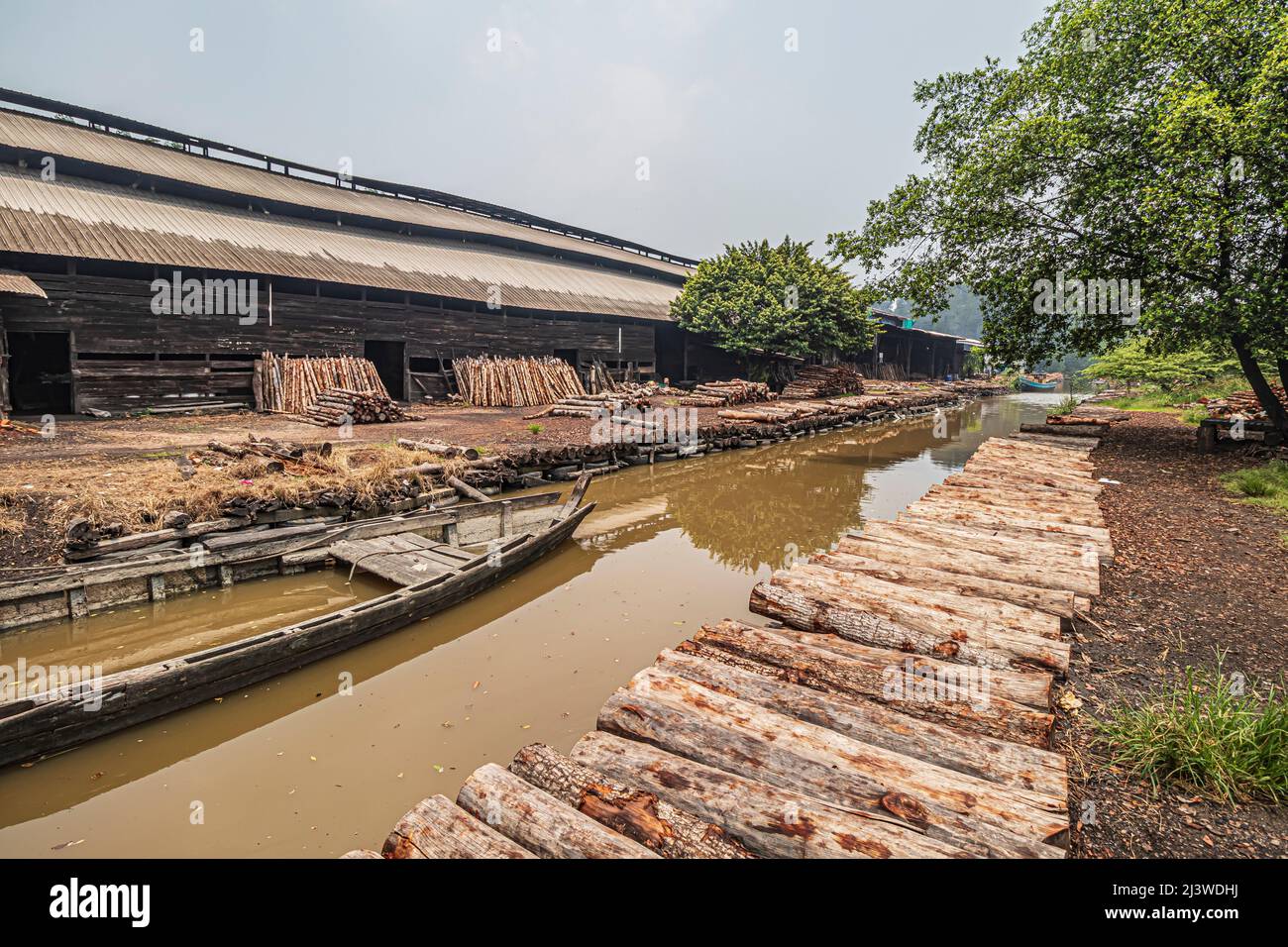 Ein Kanal und das Holzkohle-Fabrikgebäude mit Haufen Mangroven-Holzstämmen in Kuala Sepetang in Perak, Malaysia. Stockfoto