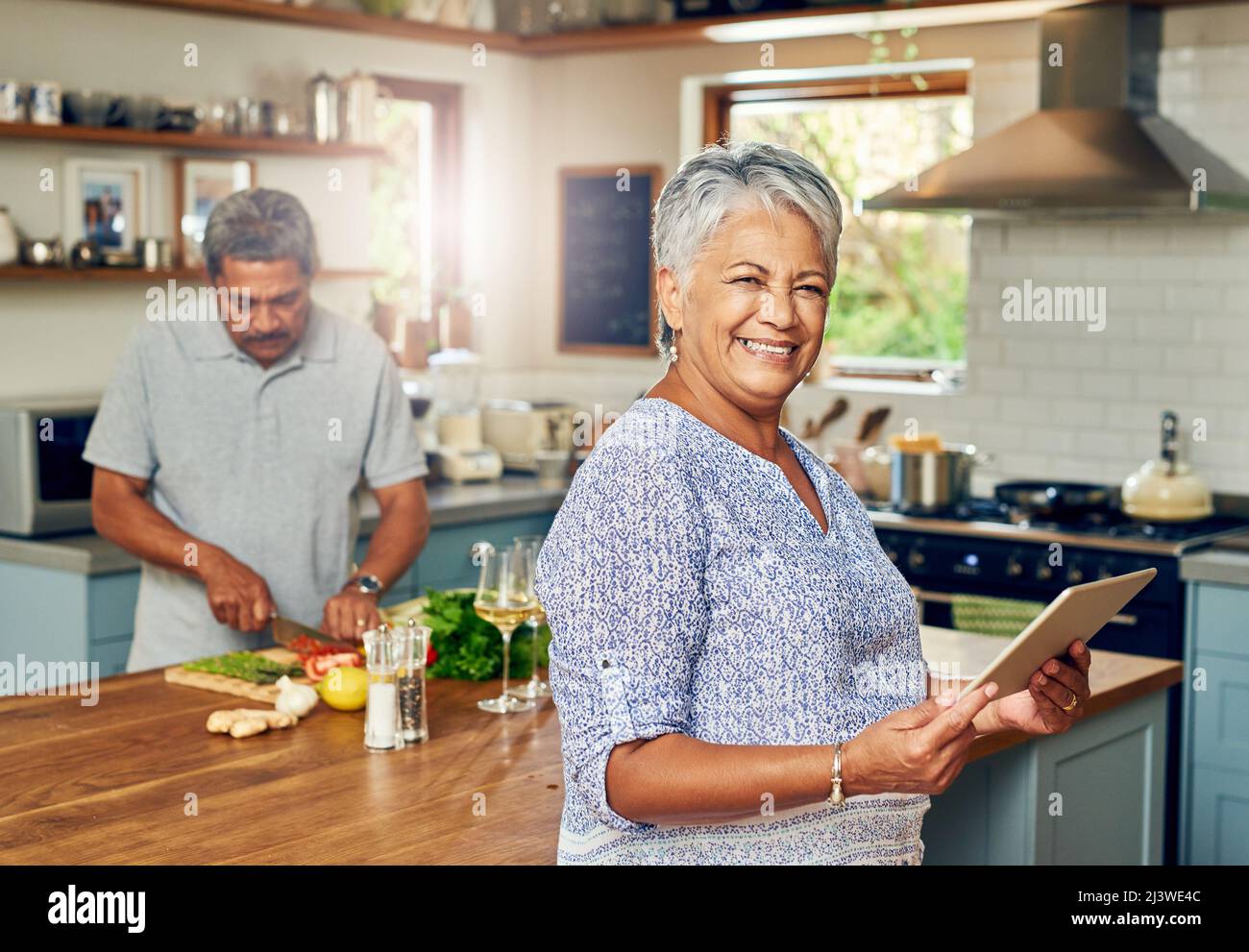 Der intelligenteste kleine Soux-Koch, den es gibt. Porträt einer reifen Frau, die ein digitales Tablet benutzt, während sie zu Hause mit ihrem Mann eine Mahlzeit zubereitet. Stockfoto
