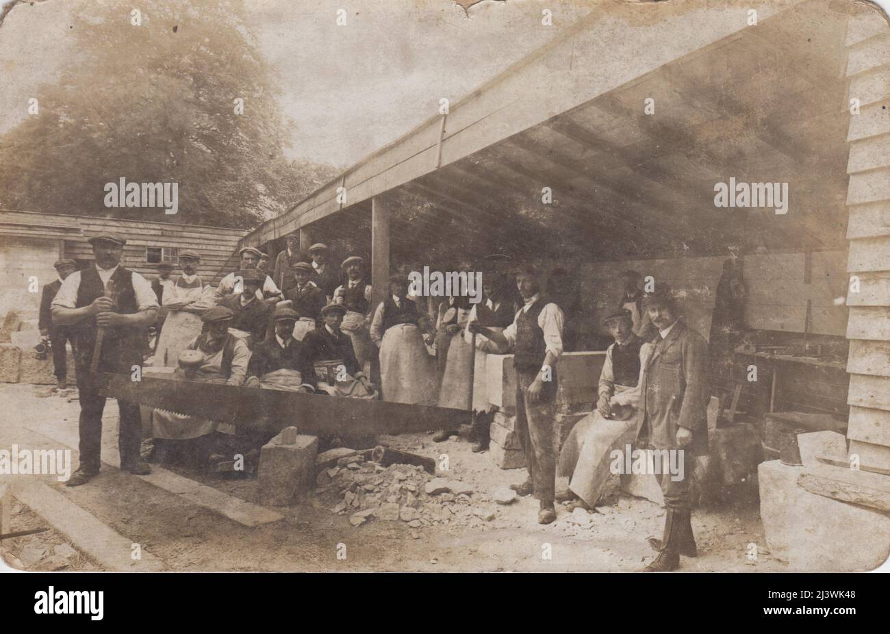 Foto von Steinmetzen in einem Hof, Anfang 20. Jahrhundert. Zwei Männer schneiden mit einer Frig-bob-Säge einen Steinblock, die anderen Männer stehen dahinter herum. Im Hintergrund sind Werkzeuge und Blöcke aus bearbeiteten Steinen zu sehen Stockfoto