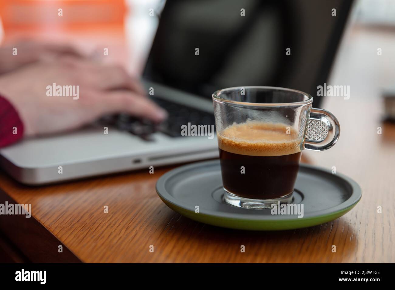 Frischer Espresso-Kaffee auf einem Holzschreibtisch aus der Nähe. Verwischen Sie am Morgen im Büro die Hände von Frauen auf einer Laptop-Tastatur Stockfoto