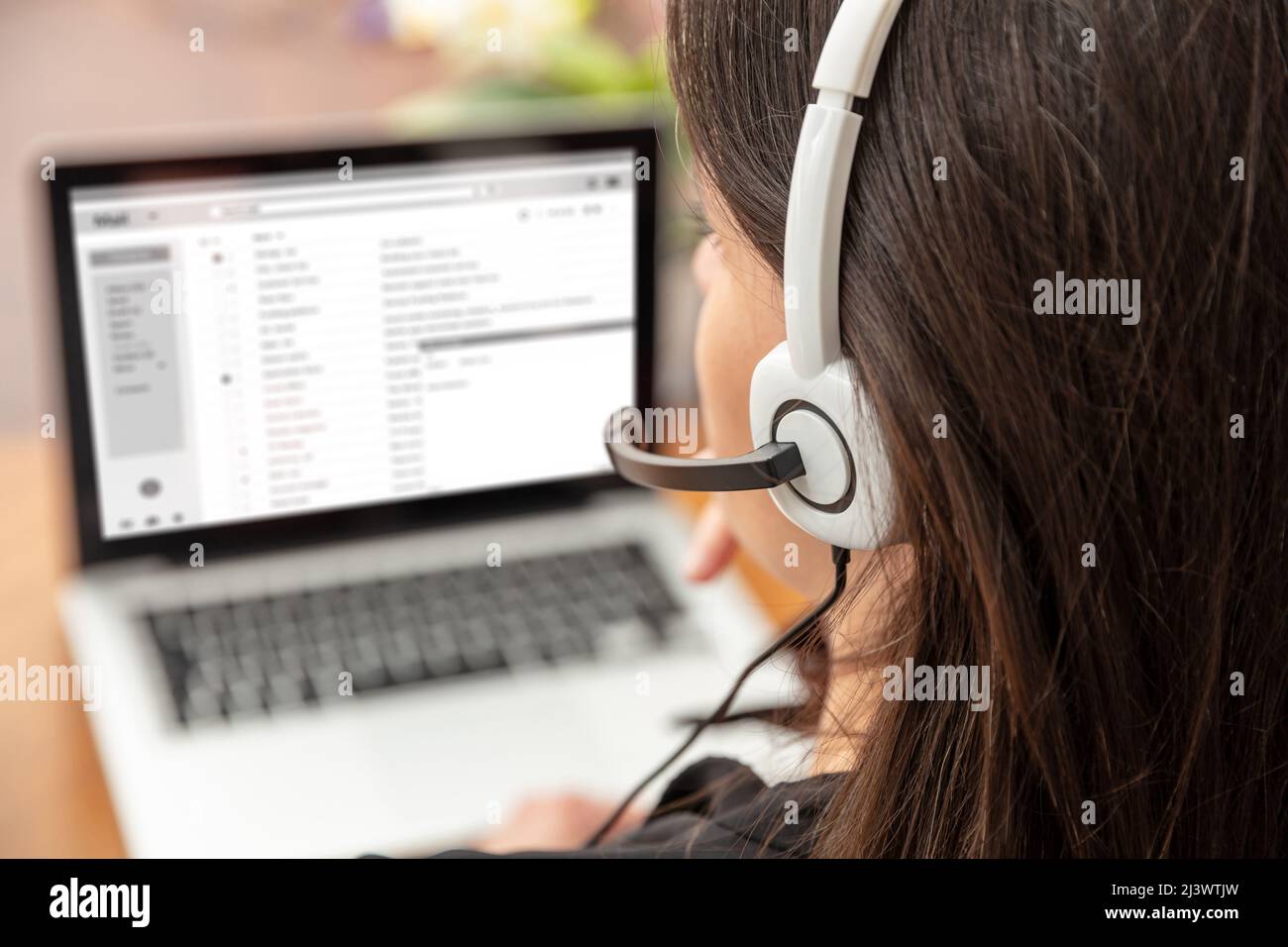 Home Office, Kundendienst, Helpdesk-Konzept. Frau mit Headset, die mit einem Laptop arbeitet, telefoniert, von hinten betrachtet. Stockfoto