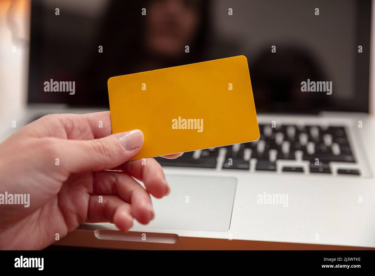 Online-Shopping, Kreditkartenzahlung. Weibliche Hände halten leere gelbe Plastikkarte und mit Computer-Laptop, Nahaufnahme, Kopierraum. Stockfoto