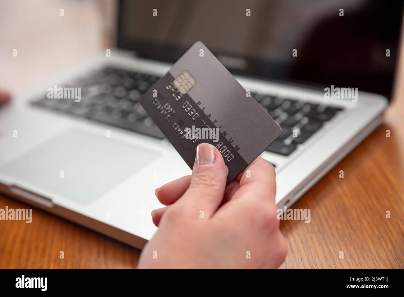 Hände mit Plastikkreditkarte und Laptop, Holztisch Hintergrund, Nahaufnahme. Online-Shopping-Konzept Stockfoto
