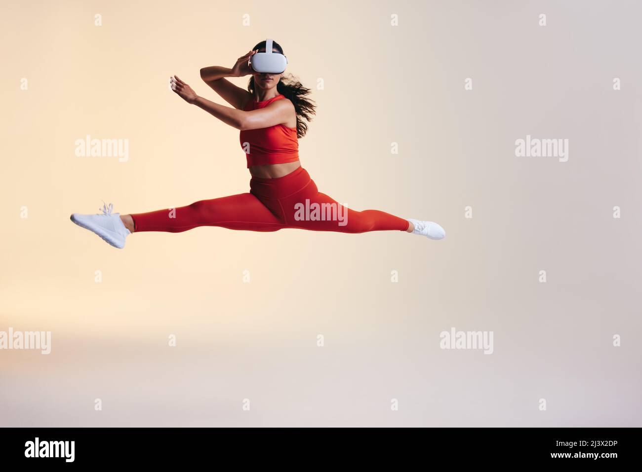 Fit junge Frau Training mit 3D Technologie. Eine athletische junge Frau springt mitten in der Luft, während sie ein Virtual Reality-Headset trägt. Aktive junge Frau explorin Stockfoto