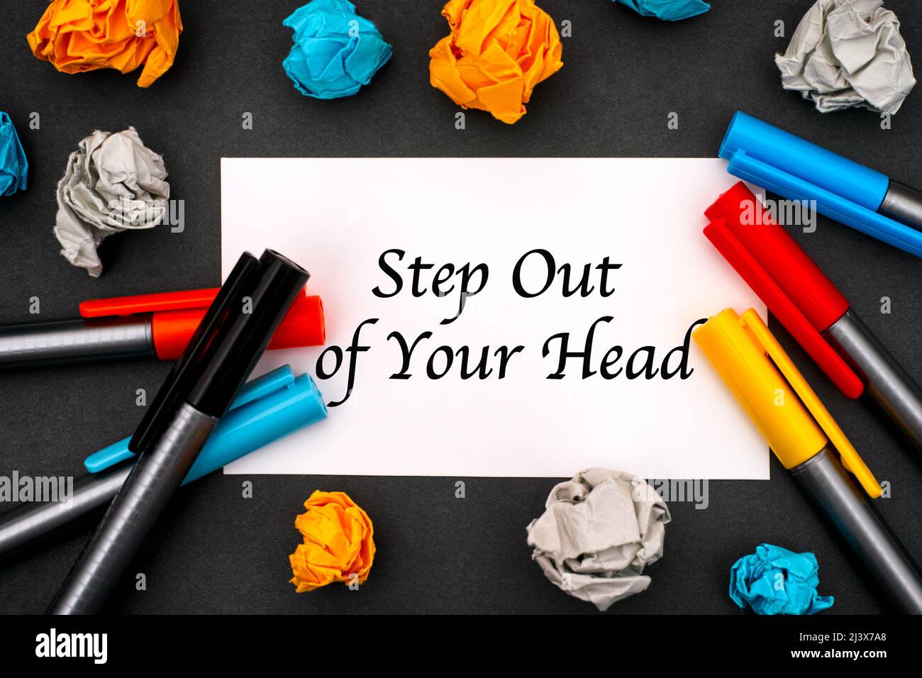 Weißes Papier mit Phrase: Treten Sie aus dem Kopf, Farbstifte und zerknittertes Papier auf schwarzem Hintergrund. Stockfoto