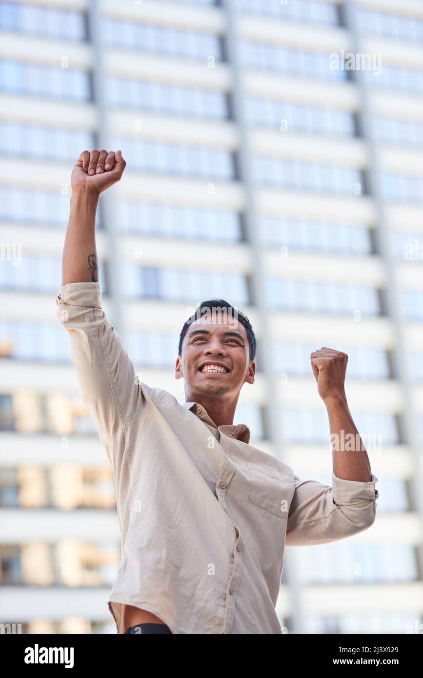 Ein junger asiatischer Geschäftsmann feiert mit erhobenen Armen vor einem Wolkenkratzer Stockfoto