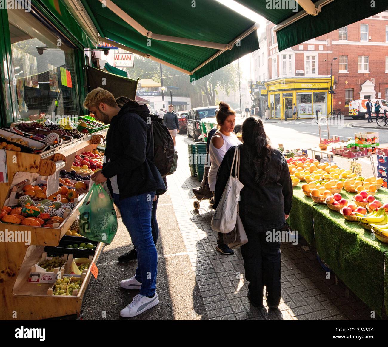 Obst- und Gemüsestände mit Canvas-Baldachin im Zentrum Londons am schönen Frühlingstag, an dem die Menschen die Produkte betrachten Stockfoto