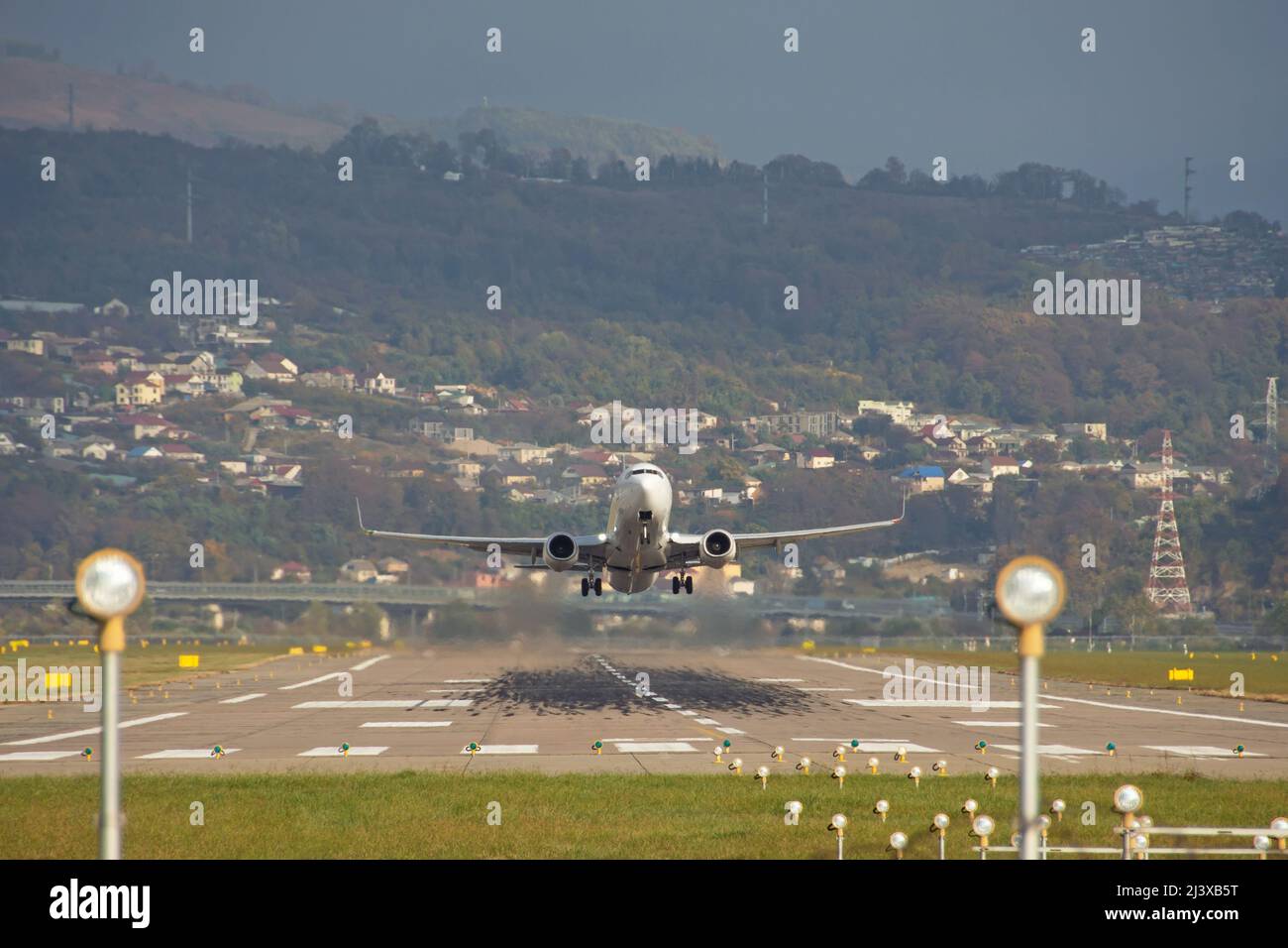 Weiße Passagierflugzeuge fliegen über die Startbahn vom Flughafen, vor dem Hintergrund von Hügeln und Häusern Stockfoto