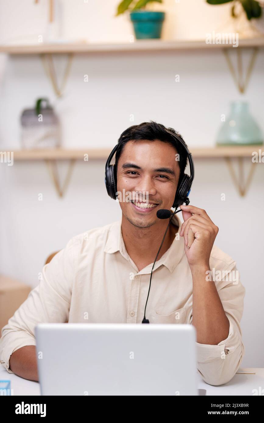 Ein junger asiatischer Mann hält das Mikrofon seines Headsets und lächelt die Kamera an Stockfoto