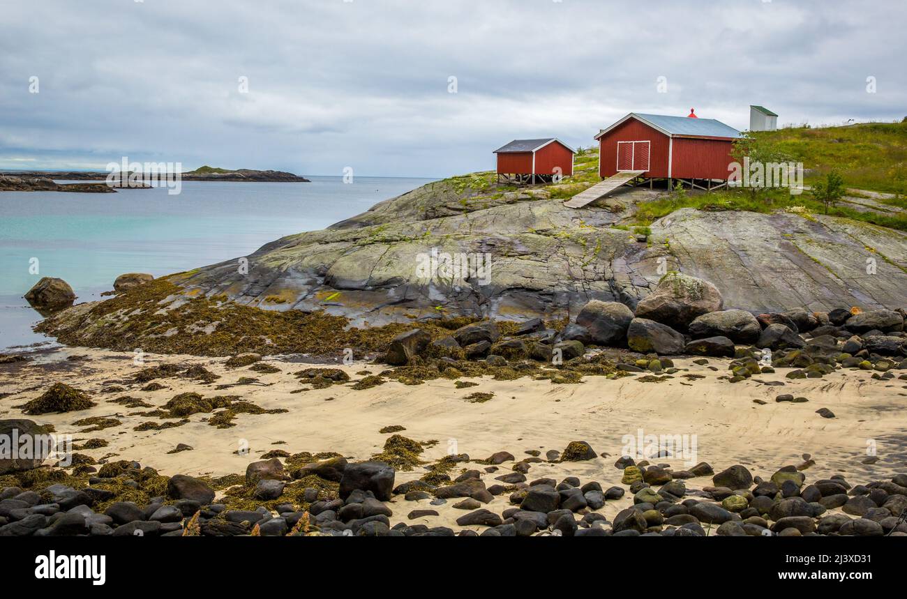 Rot gestrichene Holzbauernhäuser, die im Sommer auf Stelzen am Meeresrand auf den Lofoten-Inseln in Norwegen errichtet wurden Stockfoto