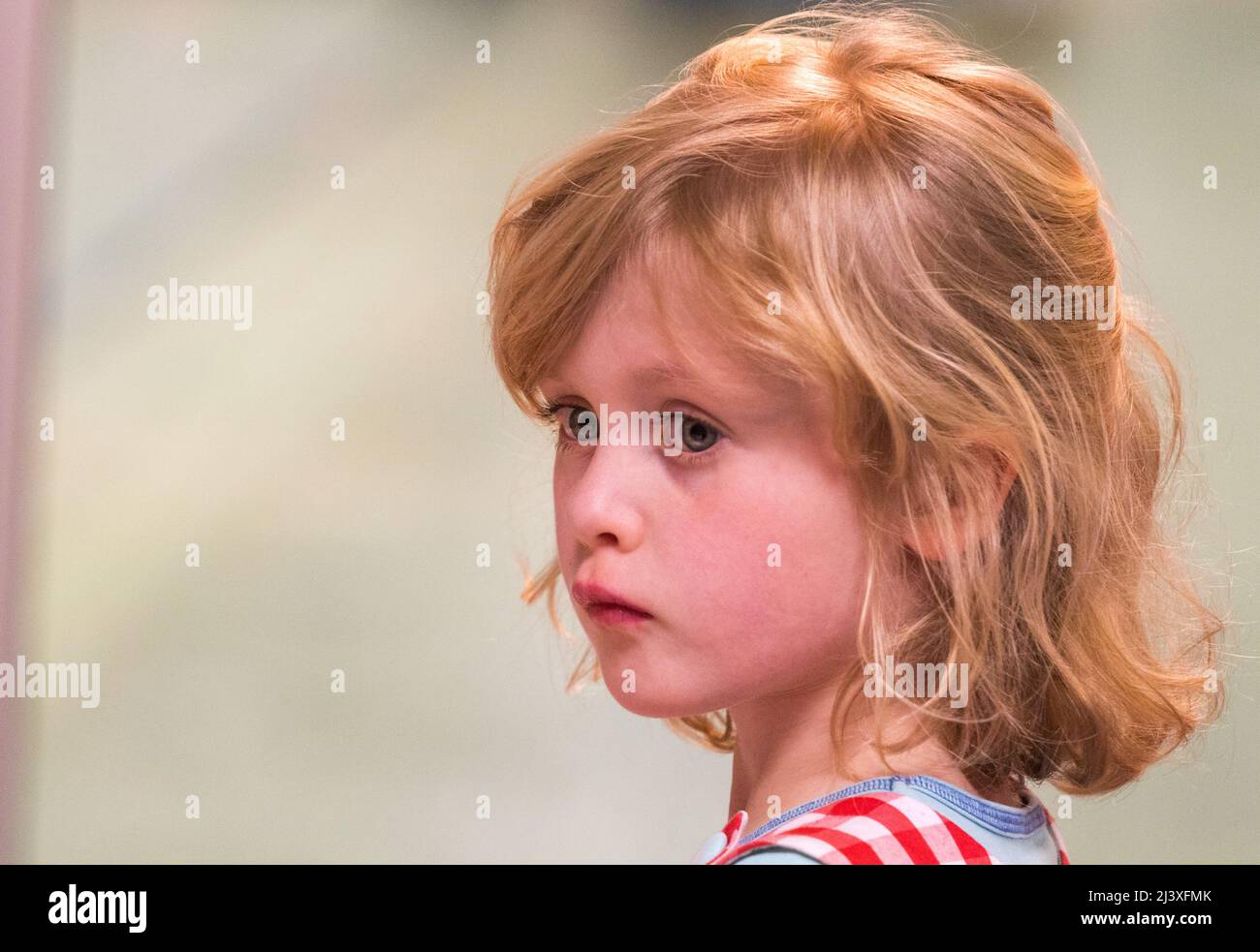 Ein Nahaufnahme-Porträt eines kleinen Mädchens mit blondem Haar und blauen Augen in einem Dreiviertel-Winkel, das nachdenklich aussieht. Stockfoto