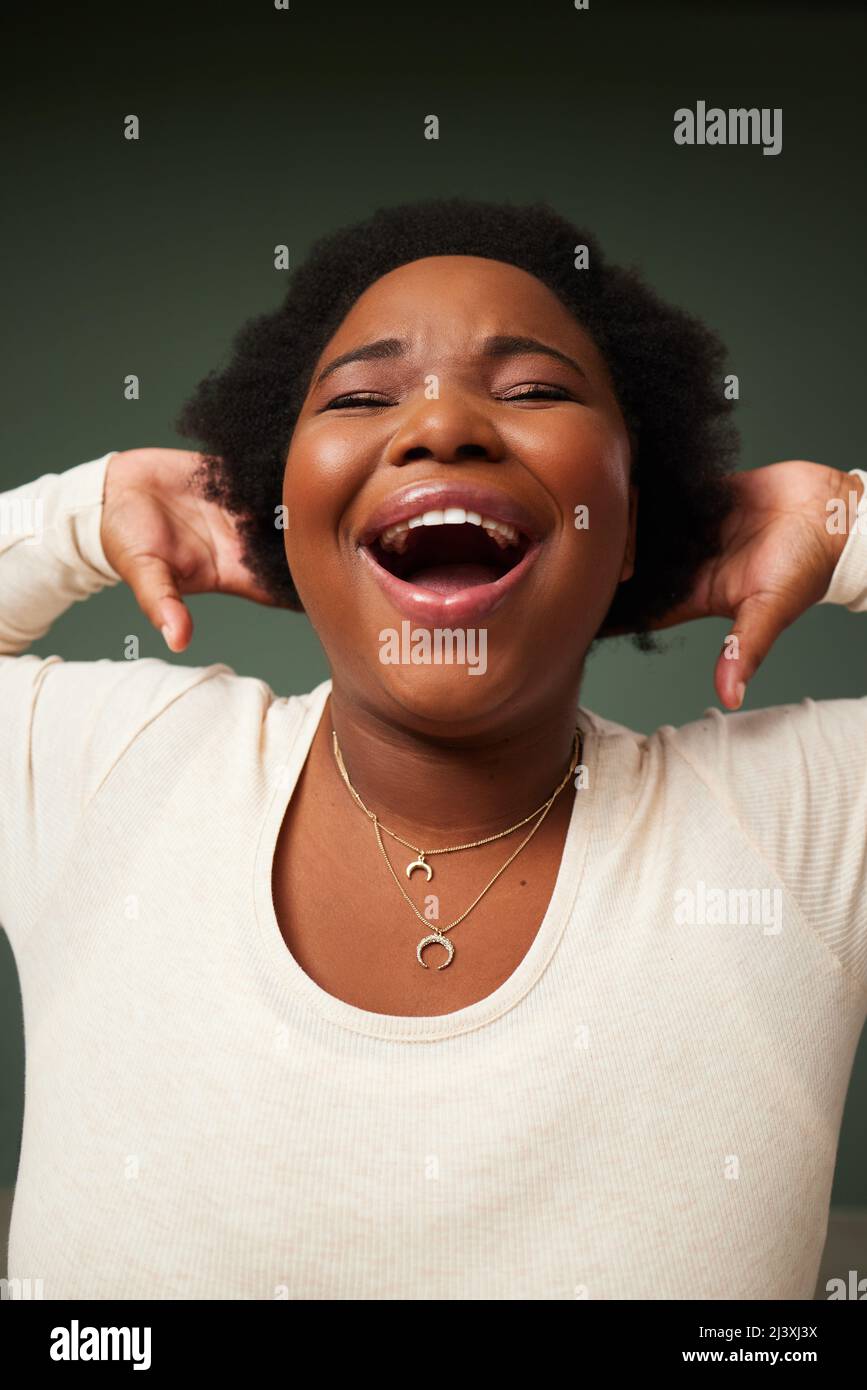 Leben, lachen, lieben. Aufnahme einer attraktiven jungen Frau, die lachend vor grünem Hintergrund im Studio posiert. Stockfoto