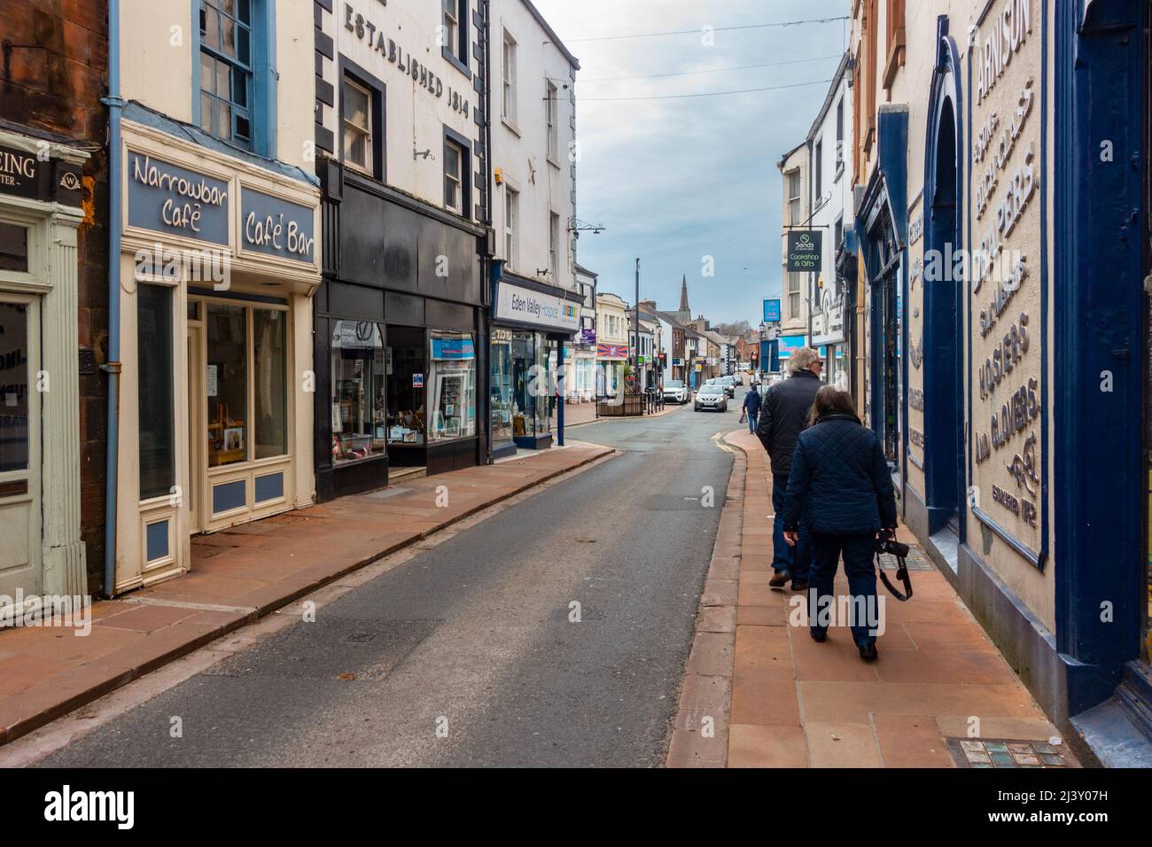 Ein Paar geht auf einem Bürgersteig entlang der Middlegate in Penrith, Cumbria, Großbritannien Stockfoto