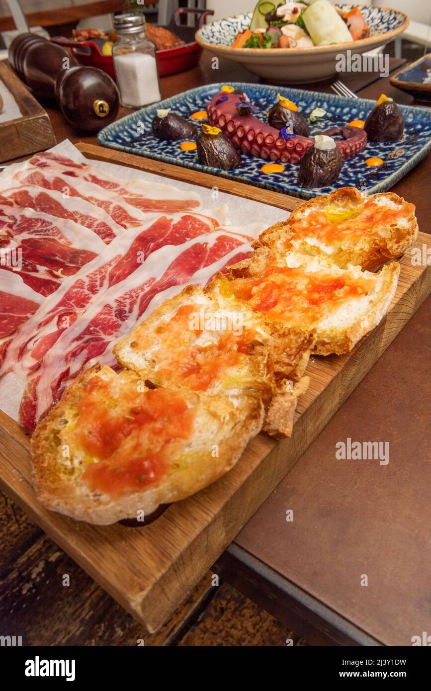 Dorfbrot Toast mit Olivenöl und zerkleinerten Tomaten, Scheiben von iberischem Schinken und Tintenfisch auf der Rückseite bedecken Stockfoto